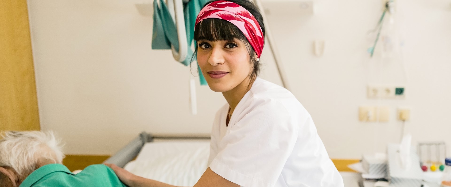 Pflegerin mit rotem Tuch auf dem Kopf im Patientenzimmer