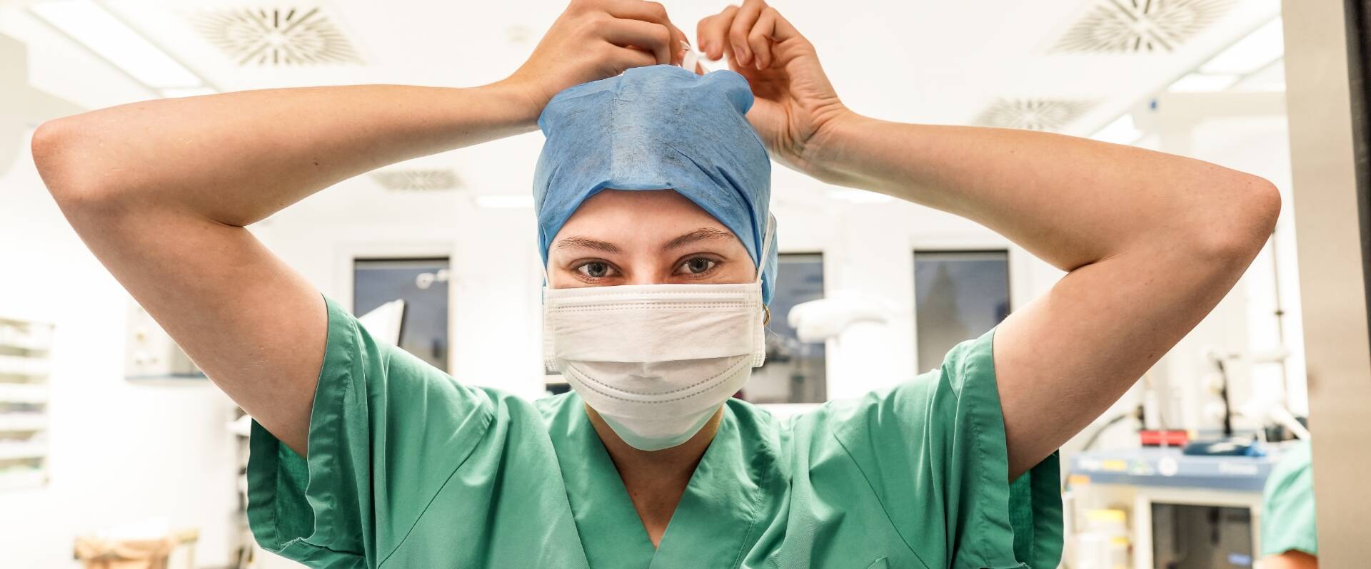 Junge Pflegekraft bindet sich Maske hinter dem Kopf zu